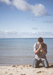 Man kneeling on knees on beach praying